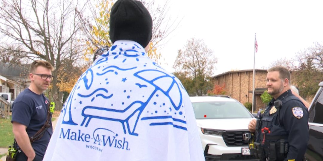 Ayden Leonhardt, seen from behind wearing a Make-A-Wish Wisconsin blanket, talks with Wausau police and fire crews during his send-off